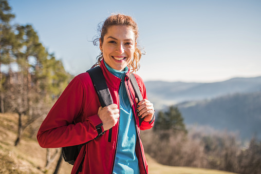 Portrait of smiling Caucasian mature woman in her 30's hiking with backpack on a beautiful day in autumn.
