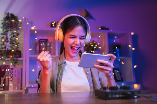 Joven asiática emocionada jugando un juego en línea en un teléfono inteligente con los puños cerrados celebrando la victoria expresando el éxito. photo