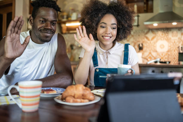 istock Friendly young afro american couple having video call using digital tablet. Smiling young black spouses join online conversation, waving hands to webcam while sitting in their kitchen. 1367787075