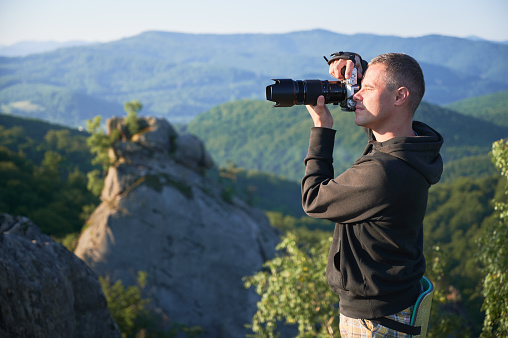 Man photographer with digital camera on top of the mountain in the morning, taking photo of sunset mountains. Concept of travel lifestyle.