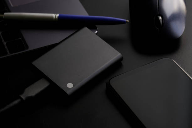 istock Smartphone and external portable SSD on a black background next to laptop or ultrabook, pen and  computer mouse. Solid State Drive. The concept of modern gadgets and information storage 1367788152