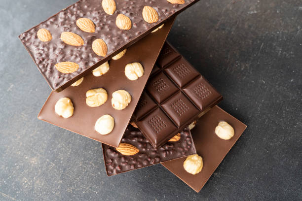 istock assortment chocolate bars with almonds, hazelnuts, handmade sweets. Composition of bars milk and dark almond chocolates hazelnuts on a black background, top view. Pastry craft on the table for chocolate background 1367796276