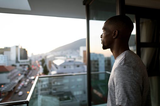 Young African man standing on balcony overlooking city at sunrise