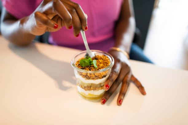 Close up young woman puts spoon into fruit and cereal breakfast