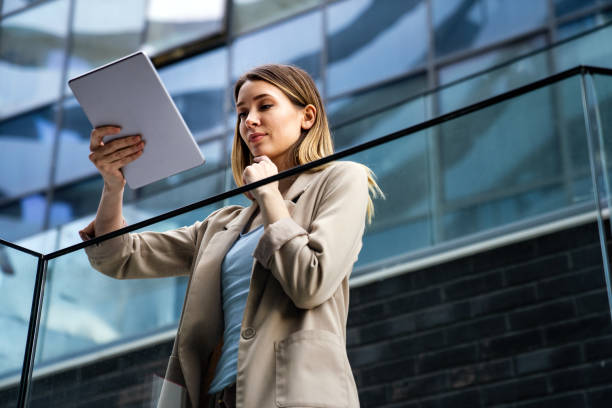 istock Successful businesswoman using a digital tablet while standing in front of business building. 1367801688