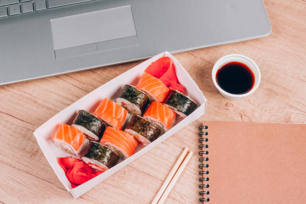 istock Different sushi rolls with salmon in delivery paper box on wooden table background with laptop. Online home order food and delivery food concept. Takeout food 1367802749