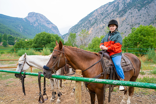 Teenager girl riding brown horse in Pyrenees valley with riding helmet