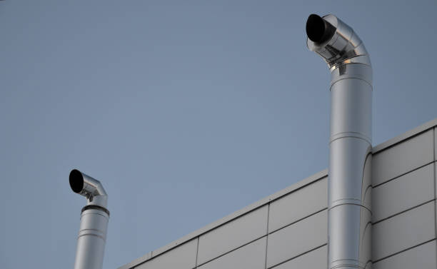 istock Industrial white building with sheet metal facade of repeating rectangle paneling. on wall are two silver-shiny chimney pipes with a curved and bevelled stainless steel pipe. gas heating turbo boiler 1367803371