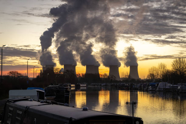 Beautiful dawn sunrise behind coal fired power station with cooling towers Beautiful dawn sunrise behind coal fired power station with cooling towers smoke plumes into sky. Global warming for electricity generation. Canal boats in foreground. climate crisis photos stock pictures, royalty-free photos & images