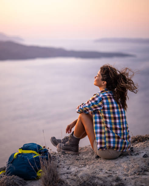 mujer relajada tomando un descanso del senderismo en una colina sobre el mar. - travel locations cyclades islands santorini vertical fotografías e imágenes de stock