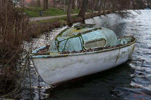 Abandoned small cabin boat made of glass fiber reinforced plastic overgrown with moss and lichen on the shore of a lake waiting for better times with new adventures, selected focus, narrow depth of field