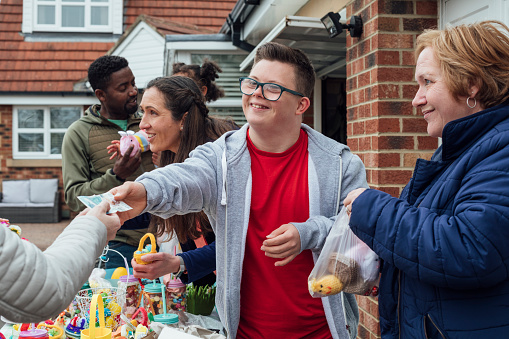 Family having an Easter yard sale in their garden in the North East of England. One of the sellers has down syndrome and is being handed money by a customer.