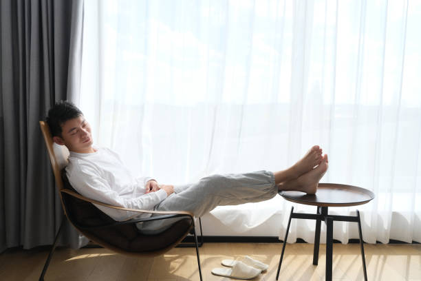 Asian young man napping on chair near window under sunshine handsome Asian young man sitting on chair resting near window under sunshine man sleeping chair stock pictures, royalty-free photos & images