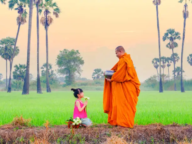 Photo of Buddhist monk going about with alms bowl to receive food and girl giving food to monk in morning in Thailand
