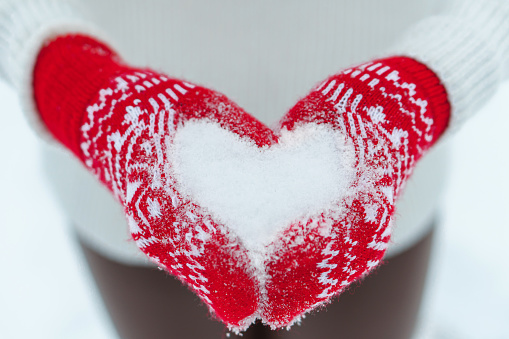 Female hands in knitted mittens with heart of snow in winter day. Love concept. Valentines day background