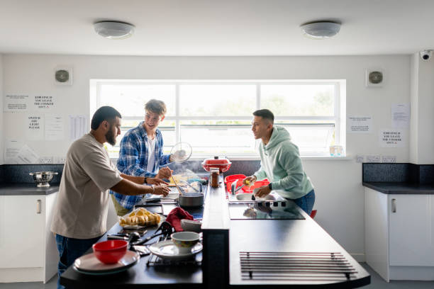 Teamwork in the Kitchen A side view shot of a small group of male uni student friends standing in their kitchen, they are wearing casual clothing and preparing a meal together. They are having a fun time. cleveland england stock pictures, royalty-free photos & images