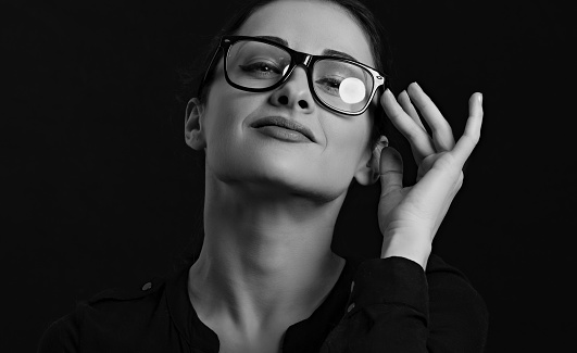 Beautiful thinking serious happy business woman  looking sure in eye glasses in casual black t-shirt on black background with empty copy space. Closeup portrait. Black and white