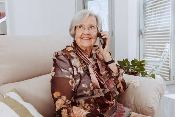 istock Old grandmother talking on smartphone sitting on couch at home 1367816021