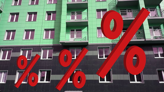 Red Percentage sign on facade background of new residential building. Interest rates. House Share. Real estate investing. Buy, sale, rental and insurance of economy class apartment in crisis. Mortgage