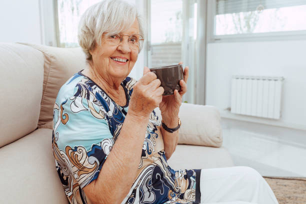 istock Elderly woman drinking coffee sitting on couch 1367816167