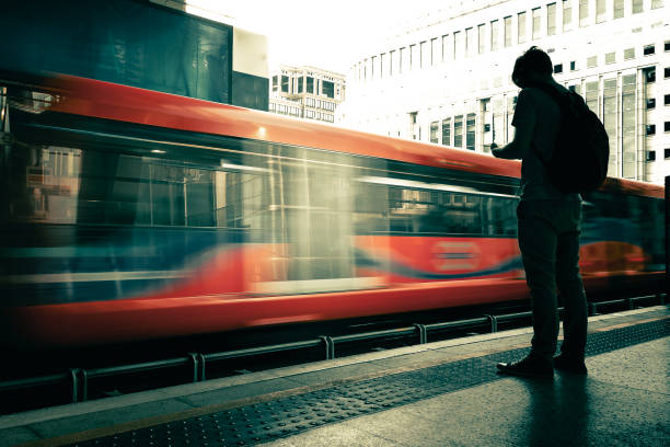 young adult commuter waiting for train on platform - blurred motion as train speeds past - docklands light railway imagens e fotografias de stock