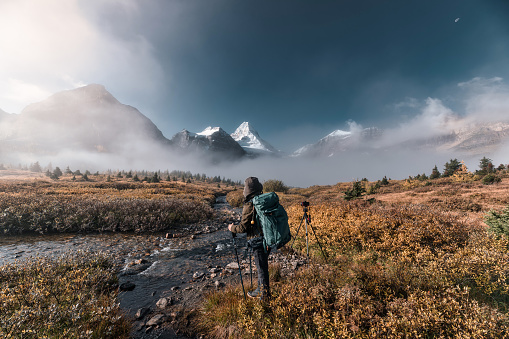 Adventure backpacker man with camera standing at mount Assiniboine in foggy on autumn forest in the morning. Assiniboine provincial park, Alberta, Canada