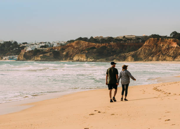 Senior couple walking on Falesia Beach in Algarve, Portugal with Albufeira visible in the background stock photo