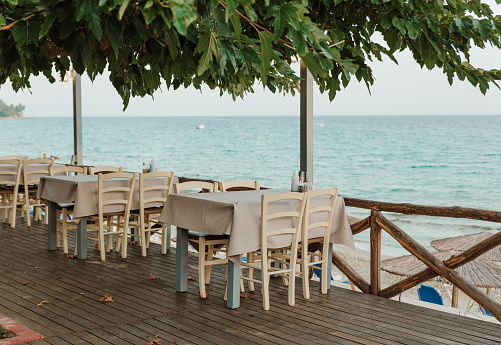 Cafe with empty tables near the sea. Open air restaraunt near sea. Greek tavern.
