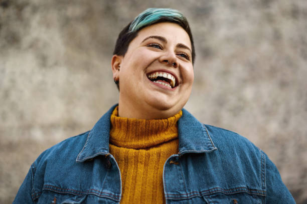 eine junge frau mit nicht-binärer sexualität lächelt und zeigt ihre zähne - trans stock-fotos und bilder