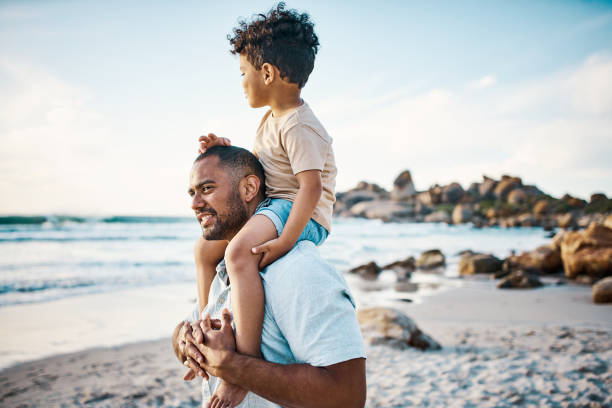Shot of a man carrying his son on his shoulders at the beach stock photo