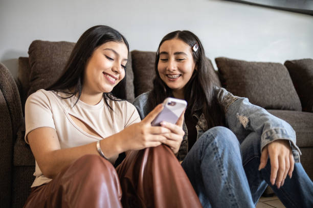 istock Sisters using smartphone sitting on the floor at home 1367822155