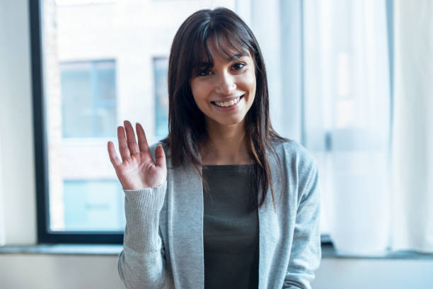 istock Smiling business woman looking at camera while waving hand at office. 1367823560