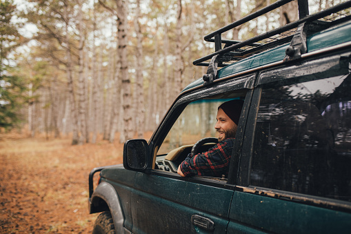 Millennial man with beard travelling off-road by car in a pine forest. Wanderlust concept.