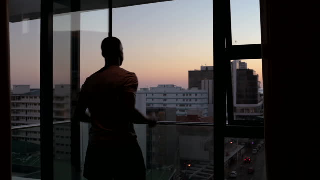 Young man warming up for jog in apartment overlooking city at sunrise
