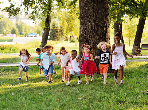 a group of preschoolers running on the grass in the Park. The concept of ethnic friendship, peace, childhood, kindness.