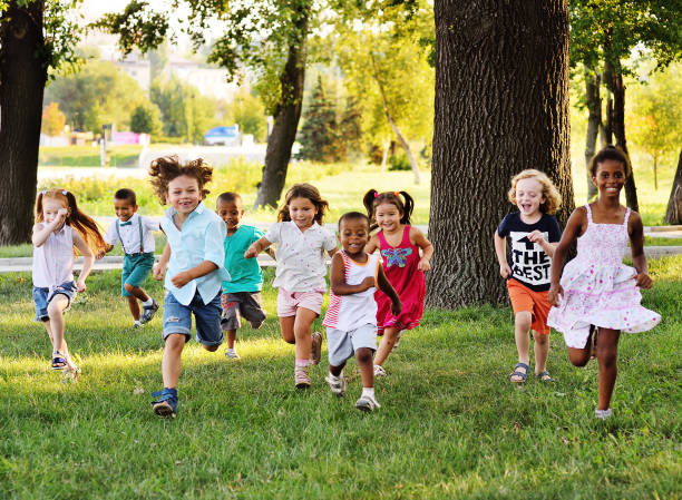 eine gruppe von vorschulkindern, die auf dem rasen im park laufen - kind stock-fotos und bilder