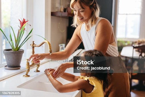 istock Mother teaching her daughter to wash her hands with soap 1367828305