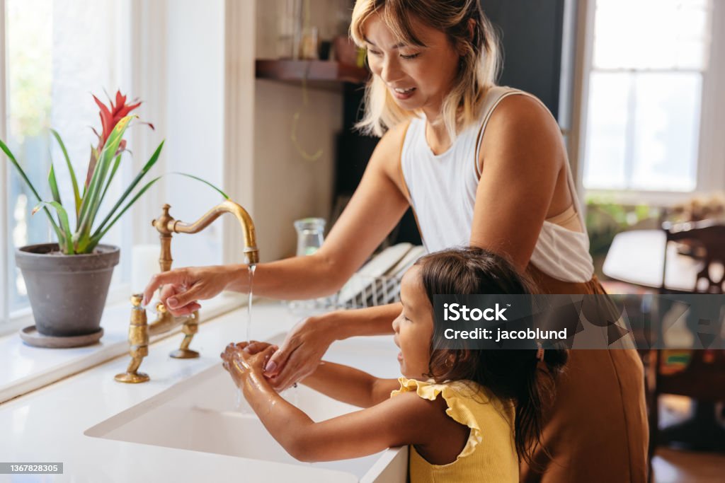 Mother teaching her daughter to wash her hands with soap Mother teaching her daughter to wash her hands with soap and running water. Loving mom following precautionary measures at home. Mother and daughter standing by the sink in the kitchen. Washing Hands Stock Photo