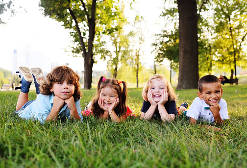 Group of school children resting on grass and smiling together in park