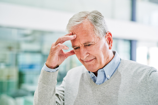 Shot of a senior man suffering from a headache at a clinic