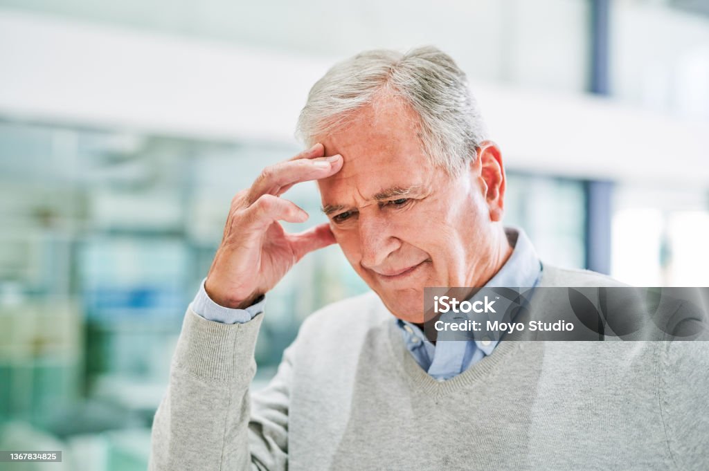 Shot of a senior man suffering from a headache at a clinic Stress can get the better of you Reminder Stock Photo