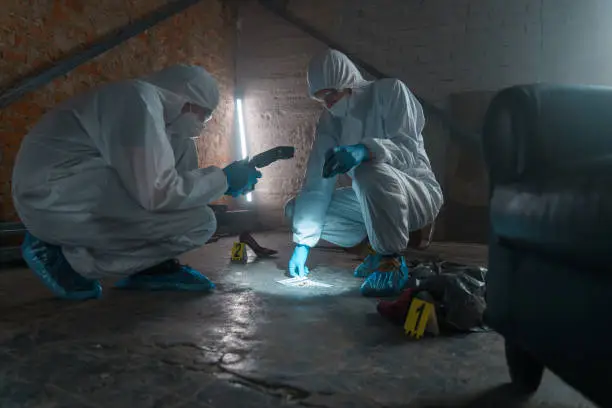Photo of Criminologists in protective suits with camera taking photos of physical evidence in a flashlight light
