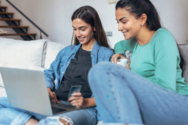 istock Two smiling young women talking while paying something online with her credit card sitting on couch at home. 1367835205