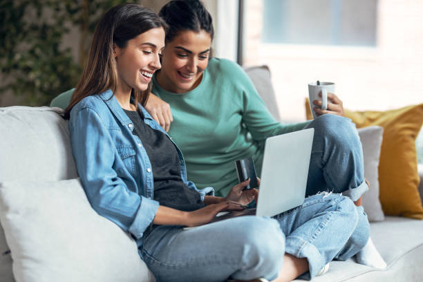 istock Two smiling young women talking while paying something online with her credit card sitting on couch at home. 1367835280
