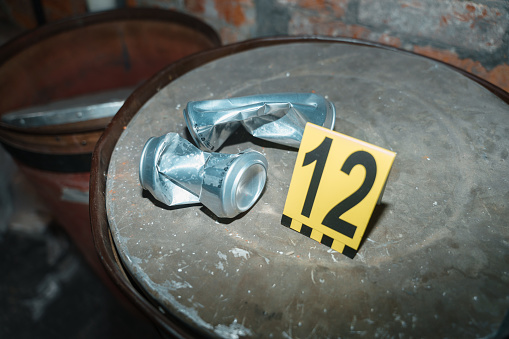 Two beer cans on an oil drum with criminologist's number next to them against the brick wall at the crime scene, we see it illuminated by camera flash