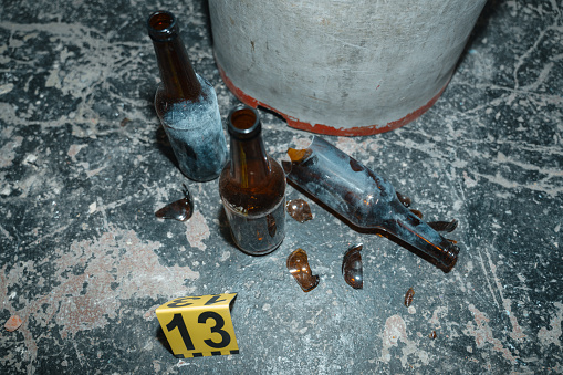 Empty beer bottles on the floor next to the oil drum at the crime scene, one of them is broken, we see it in a camera flash light