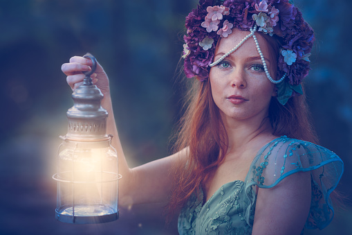 A fairy-tale or fantasy freckled red-haired girl with green eyes holding an old lantern and asking you to follow her through a dark forest.