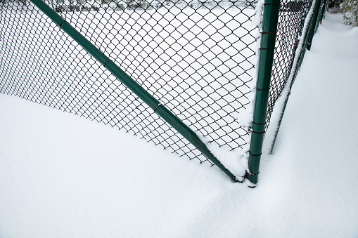 A metal fence with square cells on a snowy field. Winter abstract landscape