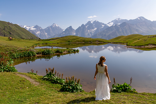 A woman in a beautiful white dress at the Koruldi Lake with a dream like view on the mountain range near Mestia in the Greater Caucasus Mountain Range, Upper Svaneti, Country of Georgia. Wedding.Bride
