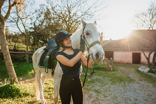Beautiful blond woman embracing her horse after riding training at a rustic stable outdoors in Majorca. Color editing and grain. Lens flares. Real life situation with a wet sweating horse. Part of a series.